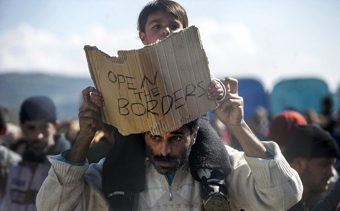 FILE: A man carries on his shoulders a child holding a banner reading "Open the borders" during a demostration of migrants and refugees protesting behind a fence and barbed wire at the Greek-Macedonian border, near Gevgelija. Picture: AFP.