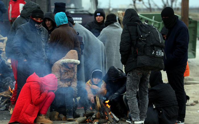 FILE: Migrants and refugees warm themselves by a fire as they wait to cross the Greek-Macedonian border, near Idomeni, on 20 January 2016. Picture: AFP.