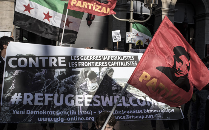 People hold the Syrian Independence flag, the flag used by the Syrian National Coalition and Syrian Interim Government and a banner reading "Against imperialist wars and capitalist borders #Refugeeswelcome" on September 6, 2015 during a rally in support of Syrian refugees at the place de la Comedie in Lyon. Picture: AFP.