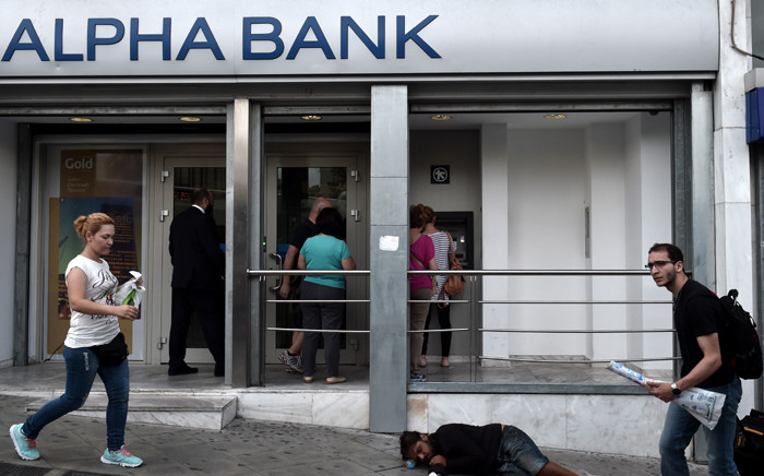 People withdraw cash from ATMs in central Athens on 19 June, 2015, as a beggar lays on the pavement. The European Central Banks decision-making governing council will hold an emergency session on June 19 to discuss a request from the Bank of Greece for an increase in liquidity to Greek banks. Picture: AFP.