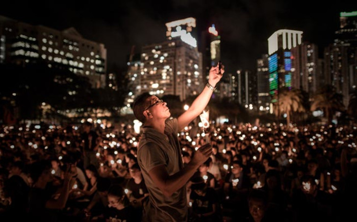 A man takes a picture with his mobile phone as people hold candles to commemorate China’s 1989 Tiananmen Square events during a candlelight vigil in Hong Kong on 4 June, 2014. Picture: AFP. 
