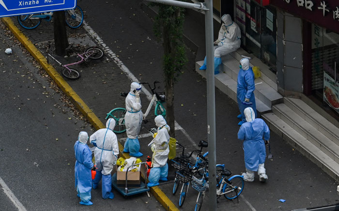 Health workers wearing personal protective equipment (PPE) stand next to the entrance of a neighborhood during a COVID-19 lockdown in the Jing'an district in Shanghai on 12 April 2022. Picture: HECTOR RETAMAL/AFP