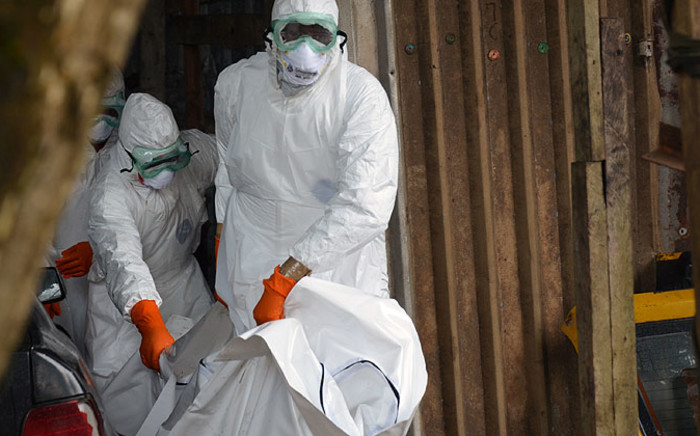 Liberian Red Cross health workers wearing protective suits carry the body of a victim of the Ebola virus out of a garage on 10 September, 2014 in a district of Monrovia. Picture: AFP 
