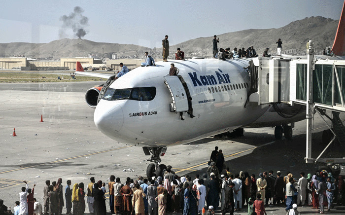 FILE: Afghan people climb atop a plane as they wait at the Kabul airport in Kabul on 16 August 2021, after a stunningly swift end to Afghanistan's 20-year war, as thousands of people mobbed the city's airport trying to flee the group's feared hardline brand of Islamist rule. Picture: Wakil Kohsar/AFP