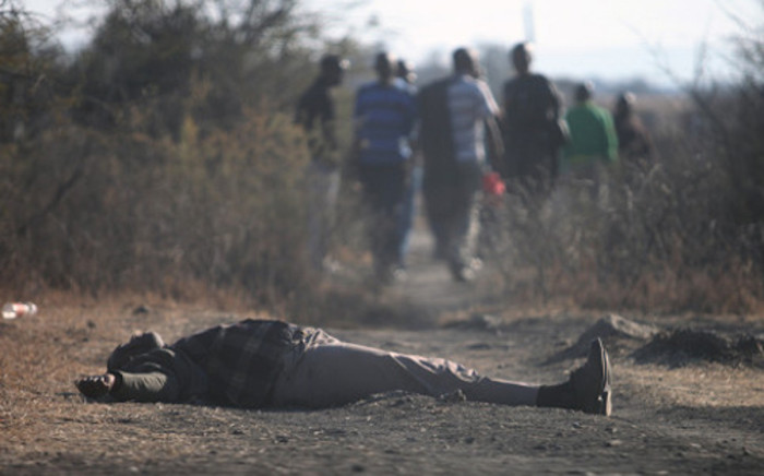 Striking Lonmin workers walk past a dead body in Marikana mine on 14 August, 2012. The area has been gripped by violence which has resulted in at least 10 deaths. Picture: Eyewitness News