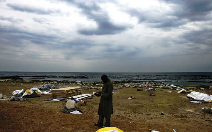 A Congolese foreign national reads a book as he walks through a damaged camp site on18 June, 2008 at a temporary refugees camp in Soetwater on the outskirt of Cape Town. Picture: AFP.