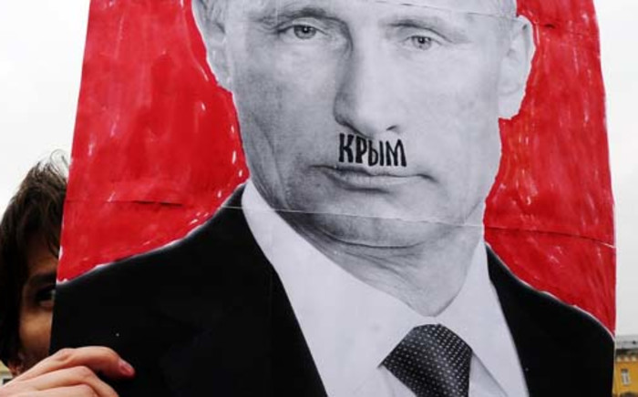 A woman holds up a portrait of Russian President Vladimir Putin with the word Crimea written above his lip, in reference to Hitler's mustache, as she demonstrates against Russian intervention in Ukraine during a rally in St. Petersburg on March 8, 2014. Picture: AFP.