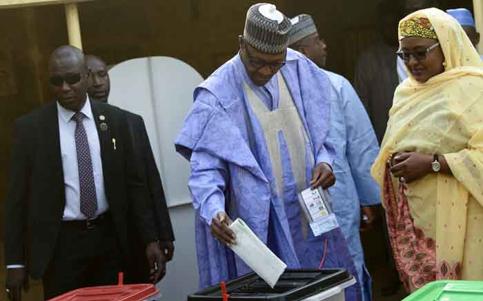 Candidate of the All Progressives Congress (APC) and incumbent President Muhammadu Buhari (C), flanked by his wife Aisha Buhari (R), casts his vote at a polling station in his native hometown Daura in Katsina State, northwest Nigeria, on 23 February 2019. Nigerians began voting for a new president on 23 February after a week-long delay that has raised political tempers, sparked conspiracy claims and stoked fears of violence. Picture: AFP