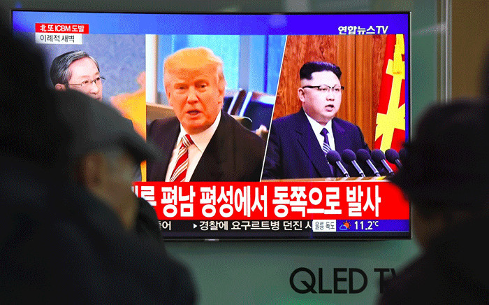 People watch a television news screen showing pictures of US President Donald Trump (C) and North Korean leader Kim Jong-Un (R) at a railway station in Seoul on 29 November 2017. Picture: AFP.