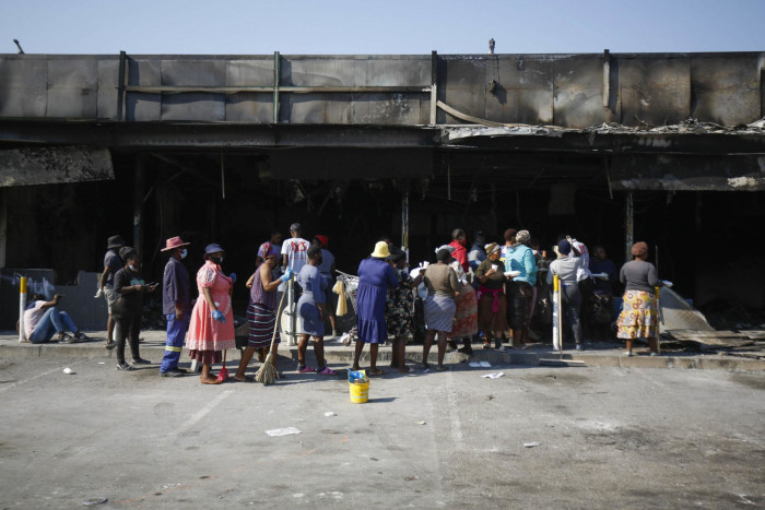 Volunteers cleaning up the gutted Dube Village Mall in Inanda, north of Durban, queue at what remains of the petrol station to have lunch on 20 July 2021.